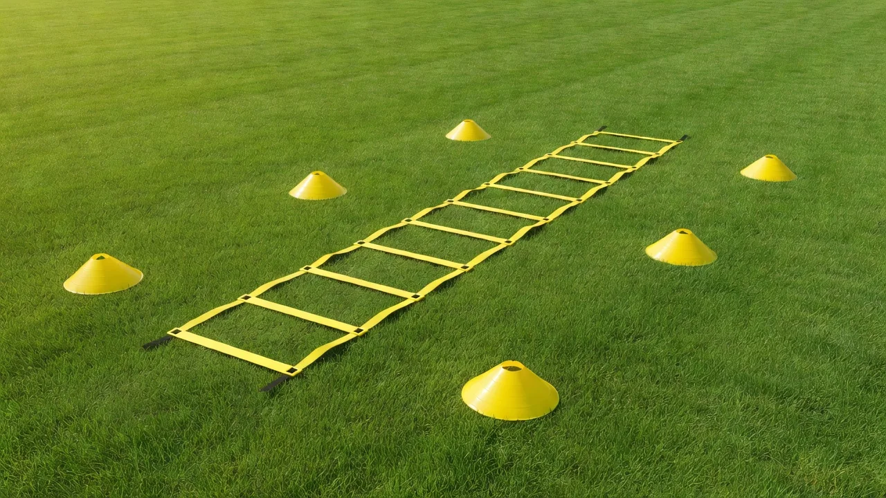 A yellow agility ladder and small hurdle cones on vivid grass