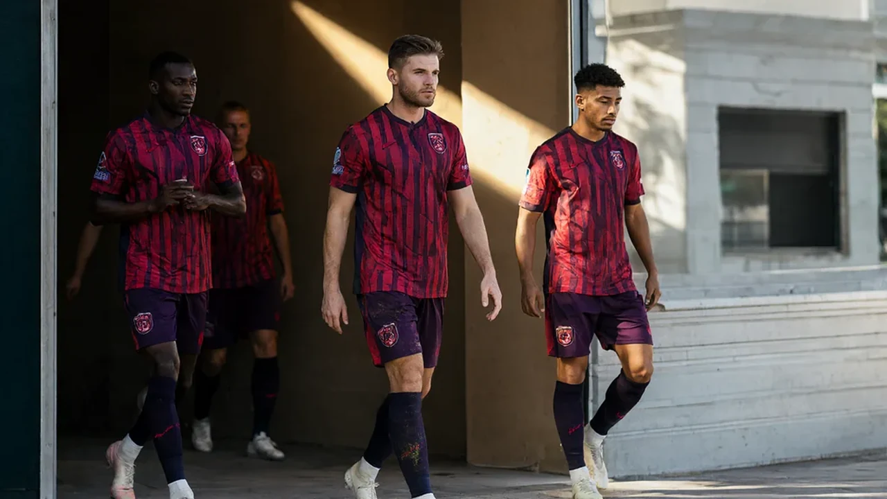 Row of plain colourful football shirts on hangers against a bright wall